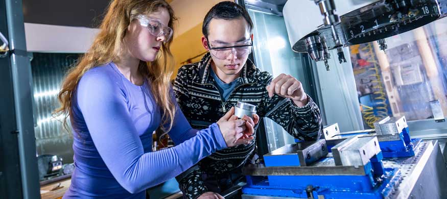 Two people wearing protective eyewear are inspecting scientific equipment